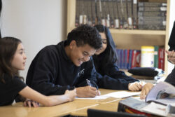 Students seated at a square table in a class room discuss a concept in seminar.