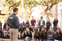 High school student speaking to a group of high schoolers outside.