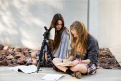 Two female students working outside on photography and design for the yearbook