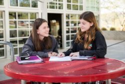 Two girls sitting at red table outside and talking.