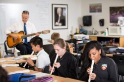 Students playing recorder and teacher playing a guitar.