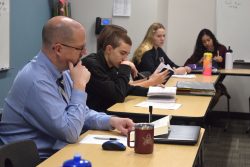 High school students sit and discuss a text with a faculty member during a seminar.