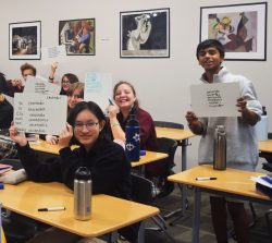 Foreign language students, seated at their desks, holding up white boards with their language translations