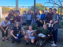 A group of students, volunteers, and the headmaster gather in the courtyard to take part in the garden club.