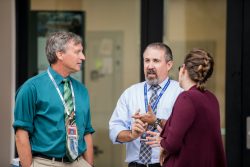 Three faculty members discuss a topic while standing outside.