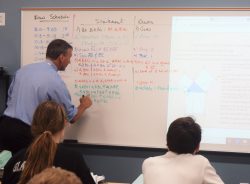 Teacher at white board explaining a math concept.